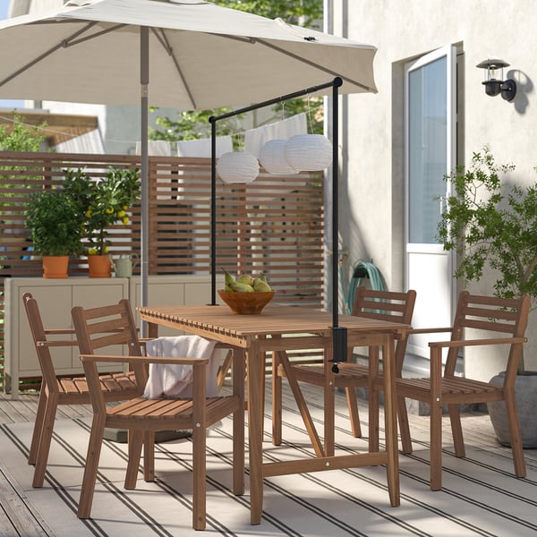 Wooden table set with 4 matching chairs, slatted tops, angled legs, shaded by umbrella. Surrounded by deck decor.