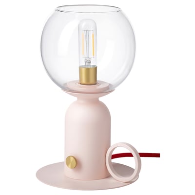 The ÅSKMULLER lamp is a sleek, modern table lamp in a light pink colour with a rounded glass shade and gold accents, giving off a warm, cosy light.