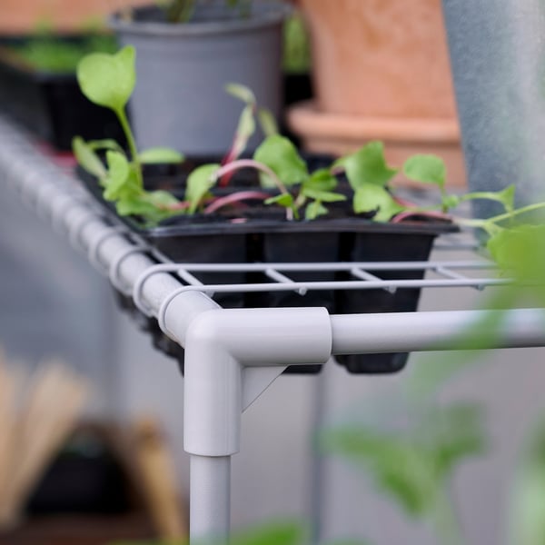 Small white greenhouse shelves hold green plant pots, promoting indoor gardening.
