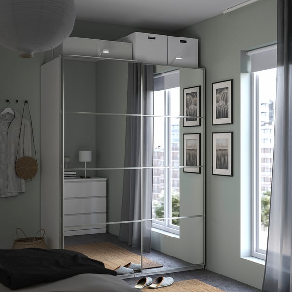 Modern bedroom with large mirror panels, white dresser, striped shirt on hanger, round lamp, and large window with light grey curtains.