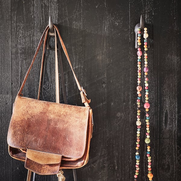 Brown leather bag hangs on hook beside beaded decorations on dark wall.