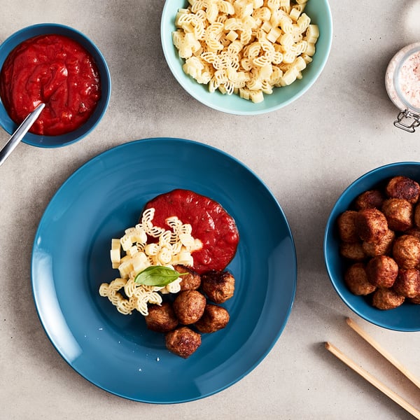 Blue plate with spiral pasta, red sauce, meatballs. Bowls of pasta, sauce, and meatballs on grey table. Ready to eat.
