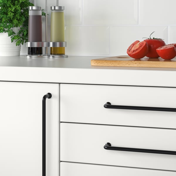 White kitchen cabinets with black BAGGANÄS handles; cut tomatoes on counter.