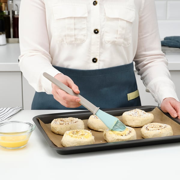 Person brushes dough with light blue brush on black tray.