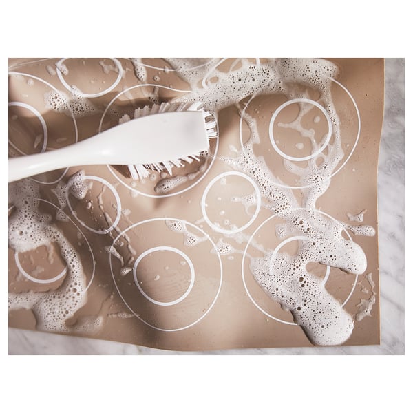 Top view of a white silicone baking mat with circular patterns for cookies or pastries, featuring a brush.