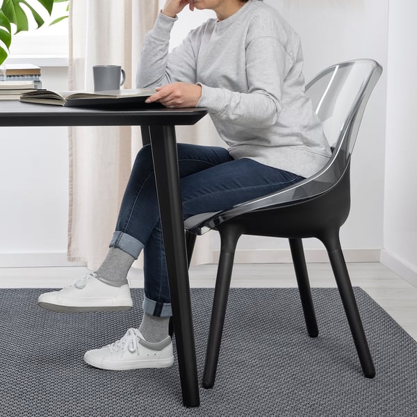 Person sitting on BALTSAR chair at table. Transparent seat, beech legs, comfortable and easy to clean.