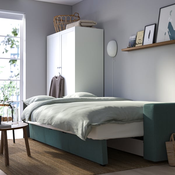 Minimalist bedroom with BÅRSLÖV sofa-bed, offering storage and quick bed conversion, against light blue wall.