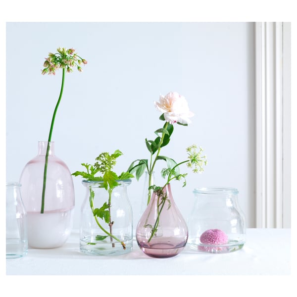 Five glass vases in pastel colours display flowers; arranged on a white table.