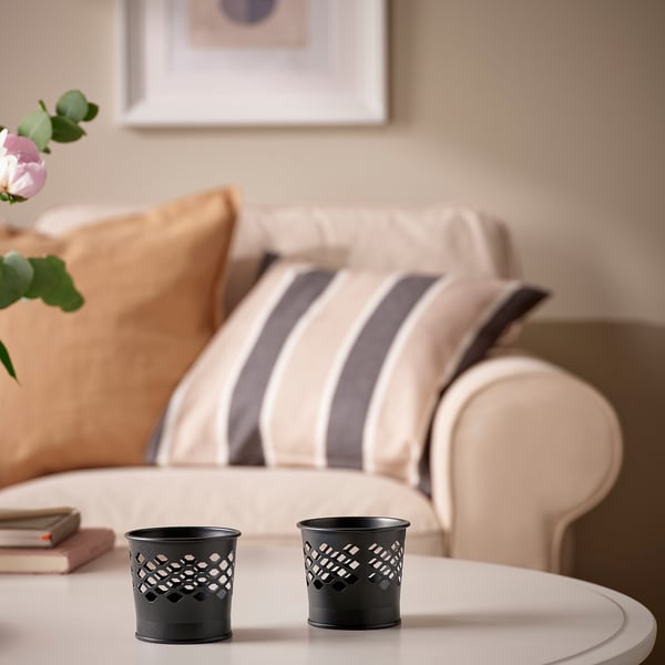 Black metal candle holders with cut-out patterns on a table, casting soft light and shadows near a cozy couch and books.