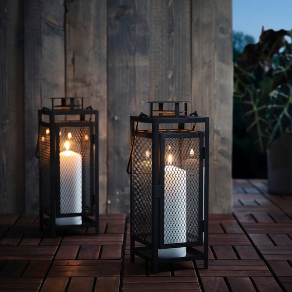 Two black metal lanterns with candles on wooden deck, illuminated, suitable for indoor/outdoor use.