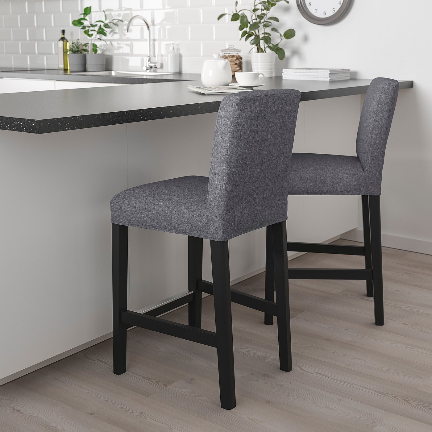 Two grey stools with cushions sit at a kitchen island with white wall and decor.