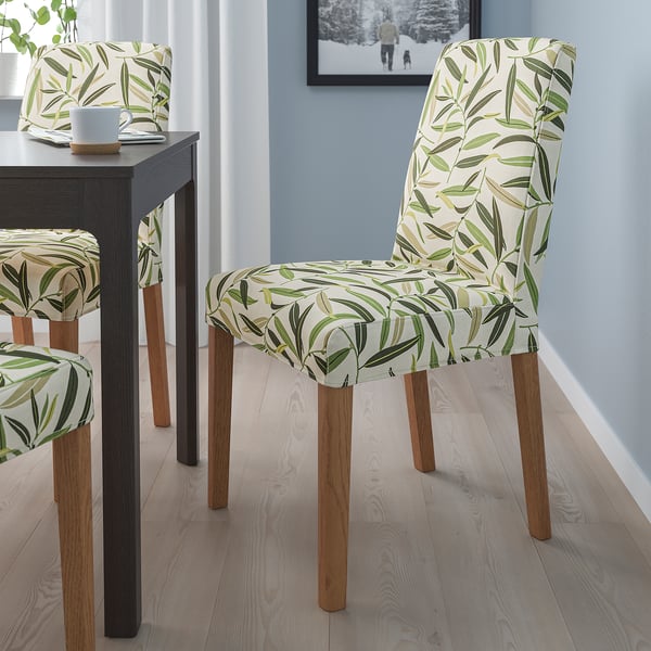 Three beige dining chairs with leaf pattern and wooden legs around a black table in a well-lit room.