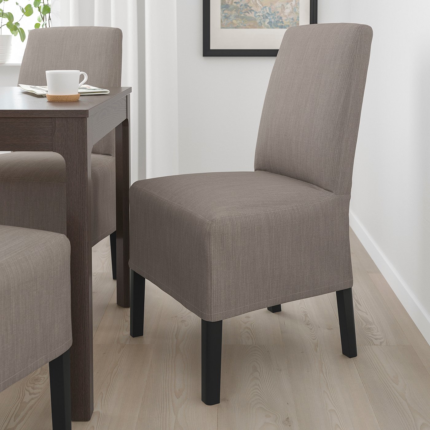 Two grey BERGMUND chairs by a wooden table. The chairs have high backs, black wooden legs, and a sleek design, fitting neatly under the table.