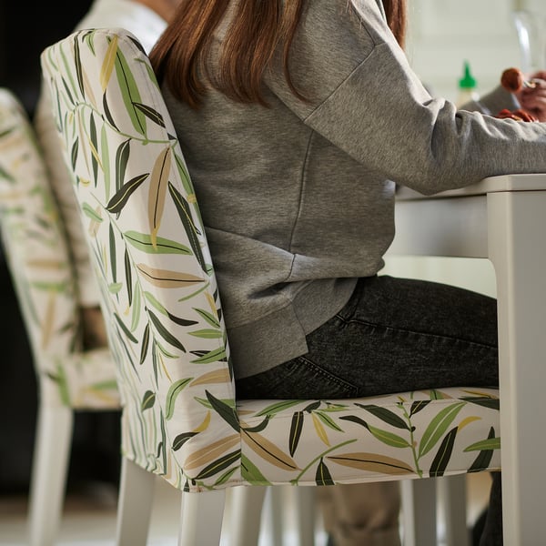 A person sits on a white BERGMUND chair with a leaf-patterned cover, wearing a grey hoodie and jeans.