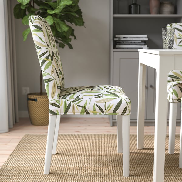 Tropical-patterned BERGMUND chair on rug, with bookshelf and plant behind.