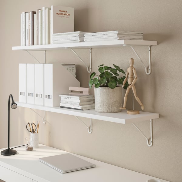 Wall-mounted white shelves with books, binders, a potted plant, and a wooden figure.