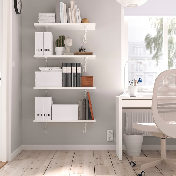 White BERGSHULT wall shelf with books, boxes, and decor. Mounted with two brackets, it fits neatly in the room corner above a desk.
