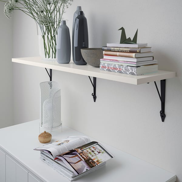 White wall shelf holds vases, books, and a lamp. Mounted with black brackets.