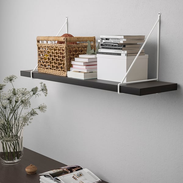 Wall-mounted shelf with black shelf and white brackets. Displaying books, wicker basket, and white box. Accented with dried flowers.