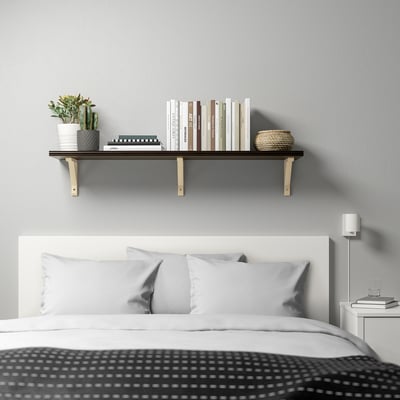 Modern bedroom with black shelf over bed displaying books, basket, cactus. Small bedside table with lamp and books.