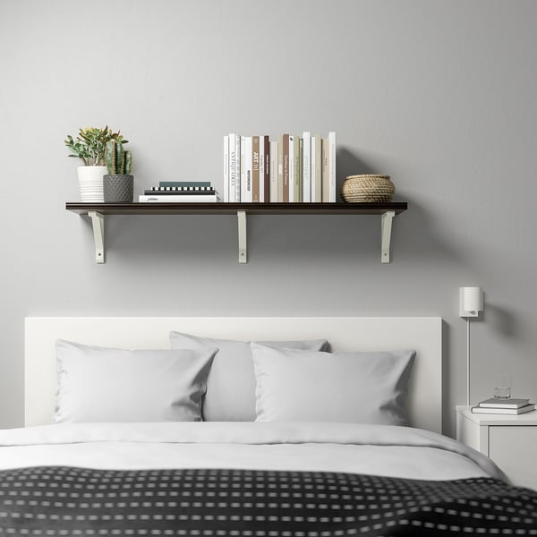 Modern bedroom with wall-mount BERGSHULT shelf, displaying books, plants, and a woven basket above a white bed with grey pillows.