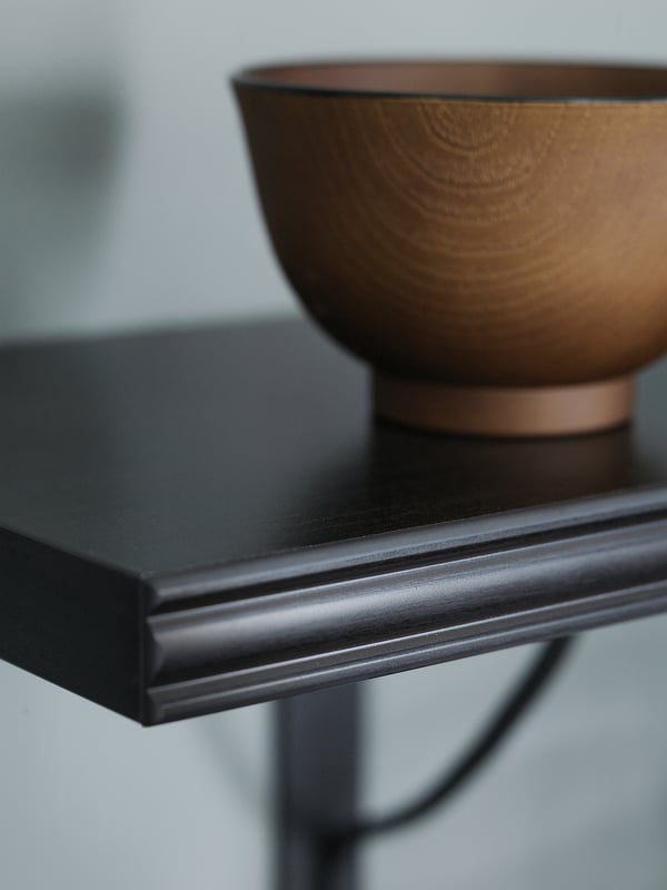 A BERGSHULT black shelf with a wooden bowl. The shelf has a smooth edge and is made of particleboard.
