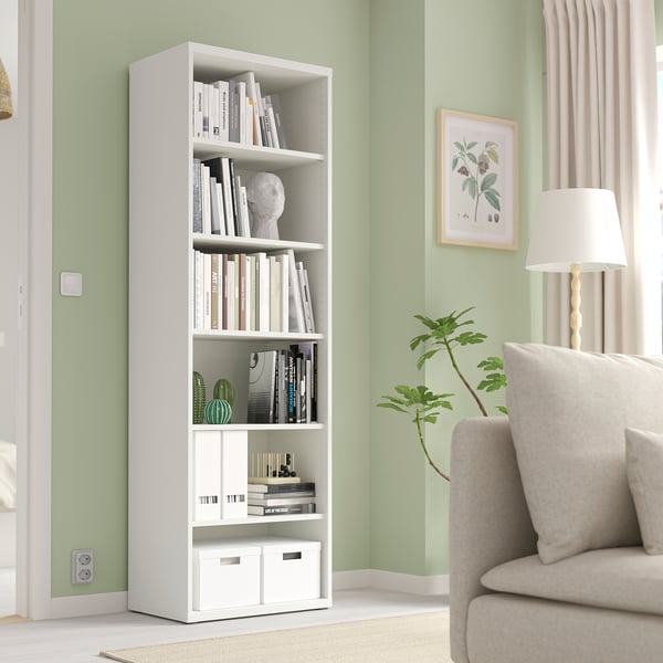Modern living room with BESTÅ bookshelf & decor. Tall, narrow, adjustable shelf. Beige armchair & lamp beside it.