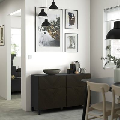 Contemporary living room with dark wood BESTÅ sideboard, pendant lights, bowl, plants, and chair.