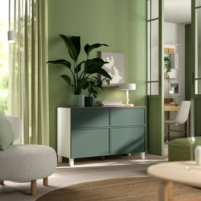 Modern living room with BESTÅ sideboard, plants, lamp, books, and art. White and green, light & airy design.