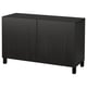 A black ikea BESTÅ sideboard with two doors. It has a sleek, rectangular shape and stands on four legs. The surface is smooth and the doors are flat.