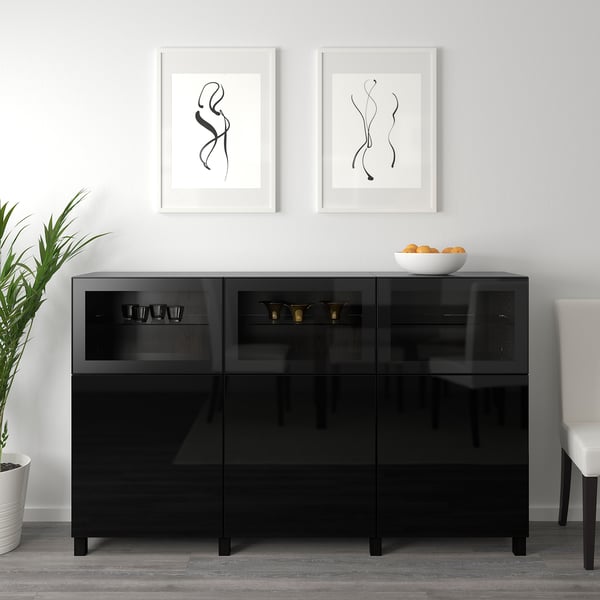 Modern black sideboard with glass doors displays glasses and dishes. Artwork and fruit bowl atop.
