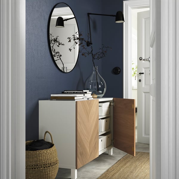 BESTÅ sideboard with open door and adjustable shelves. Dark blue wall, mirror, basket, books, vase.