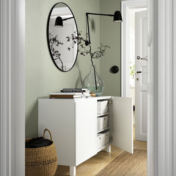 Small, stylish storage sideboard with a mirror, books, vase, and a basket by the door, exploring storage and decor functions.