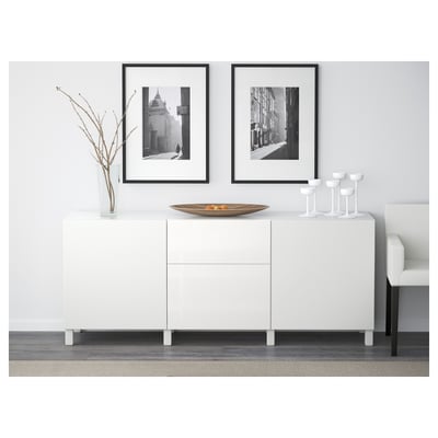 White storage unit with drawers and shelves, styled with decor items. Framed photos hang above.