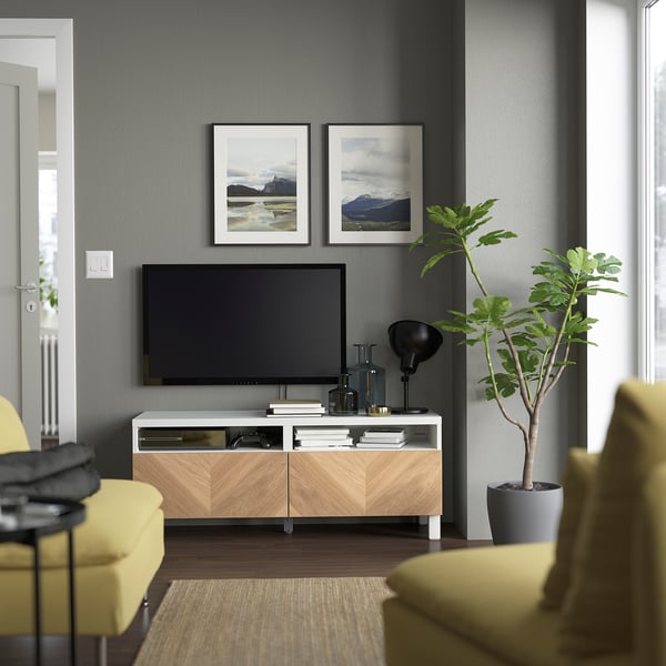 Modern living room: BESTÅ tv stand in white/beech, holding tv. Yellow chairs, grey wall, plant. Photos, lamp, books on stand.
