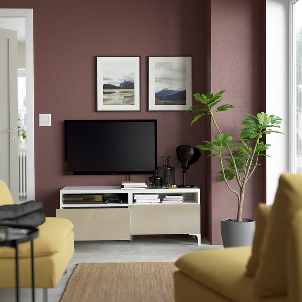 Modern living room with BESTÅ tv stand: flat-screen tv, two framed mountain photos, yellow armchairs, potted plant, and black lamp.