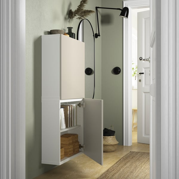 White BESTÅ cabinet with one door open, displaying baskets and books. Black adjustable wall lamp above.