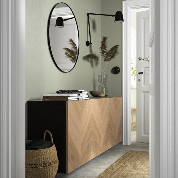 Wooden BESTÅ cabinet, chevron pattern, black accents, lights, mirror, sage green wall.