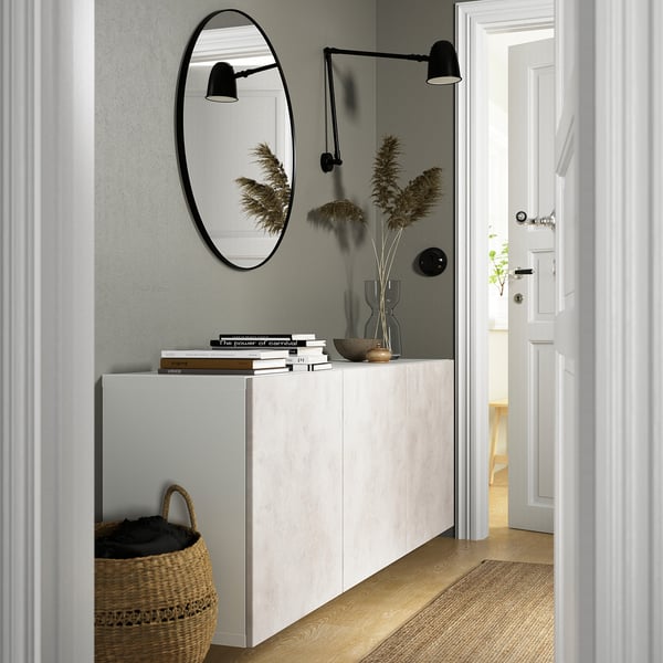 White BESTÅ cabinet with shelves & doors, wall-mounted, flanked by black lamps, books, and decor with a mirror and basket.