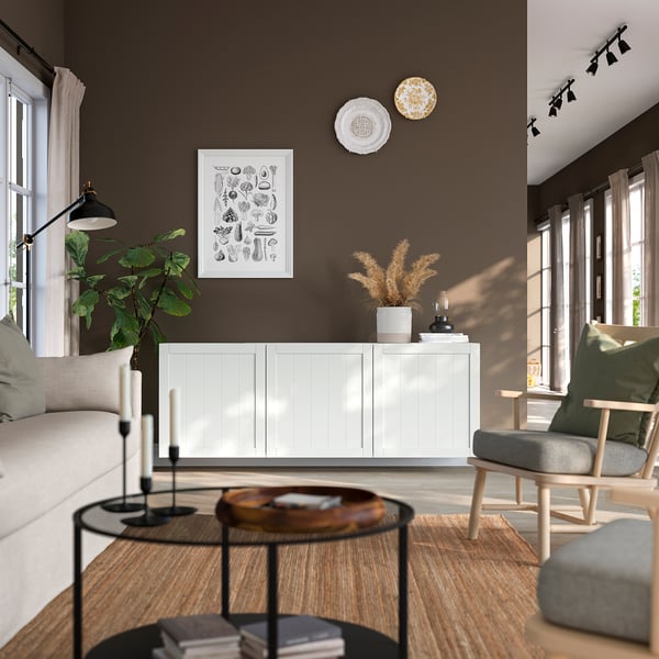 Modern living room with BESTÅ white cabinet, creating airy feel. Its large, housing books & plants, between windows & light fixtures.