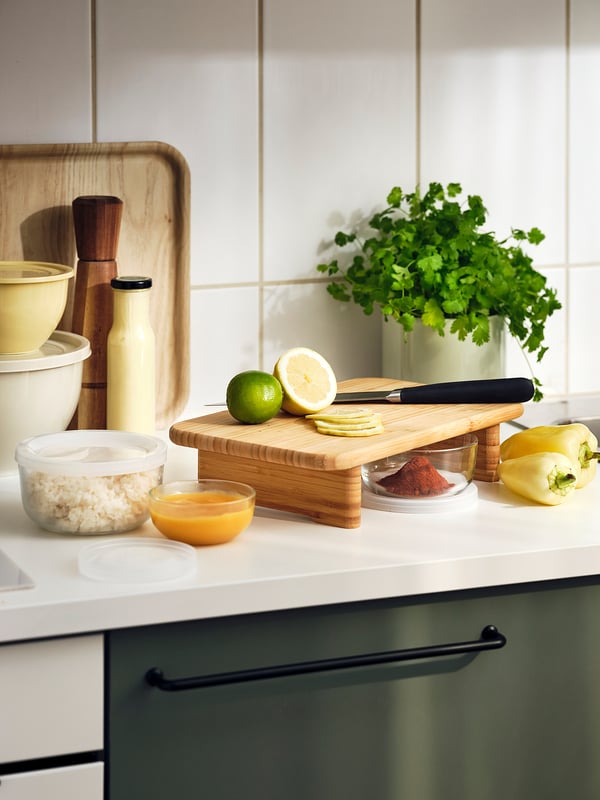 A modern kitchen counter BESTÄMMA glass food containers in yellow and clear, with ingredients like citrus fruits, spices, and coriander.