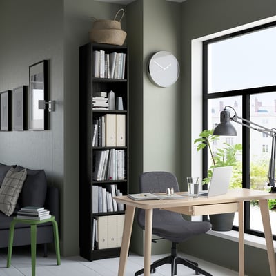 Modern home office with BILLY bookcase, desk, clock, and city view.