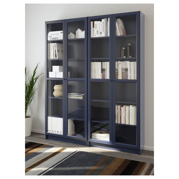 Blue BILLY bookcase with glass doors, holding books and decor items, positioned against a wall.