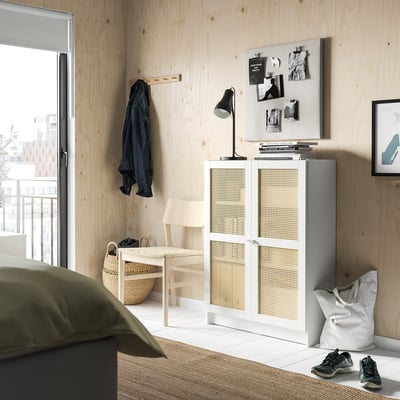 Modern bedroom with light wooden wall, white cabinet, black coat, and green blanket.