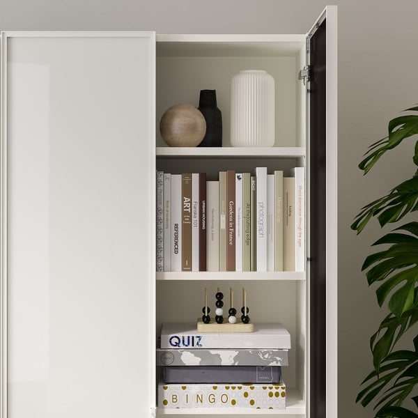 White BILLY bookcase with glass doors, displaying books, decorative objects, and games. Shelves are adjustable.