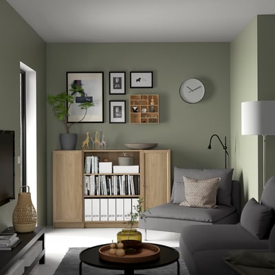 Green living room with grey sofa, BILLY bookcase, clock, and coffee table.