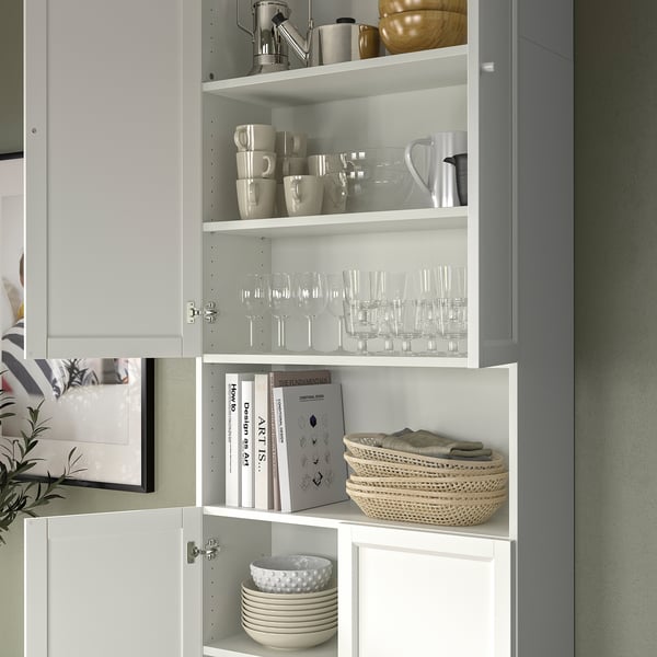 Neatly organised grey and white BILLY bookcase with glassware, mugs, books, and basket. Simple and modern design.