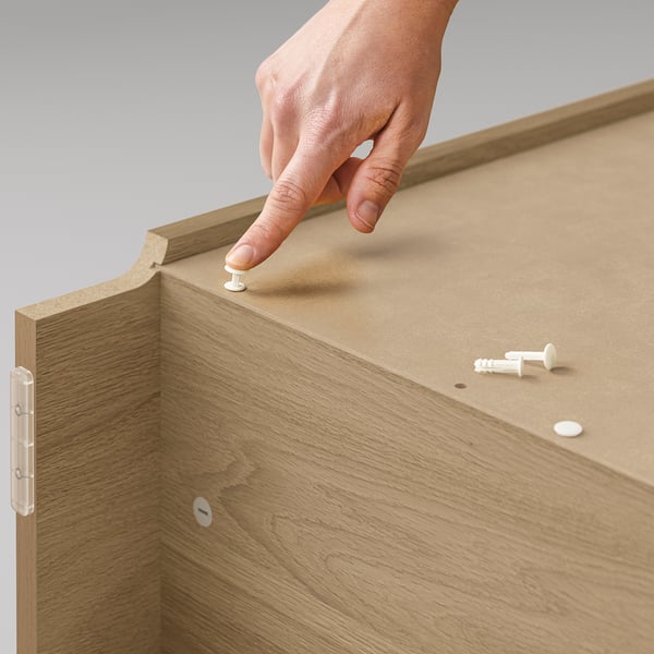 A hand assembles BILLY bookcase, light brown, wooden texture, adjustable hinges visible.