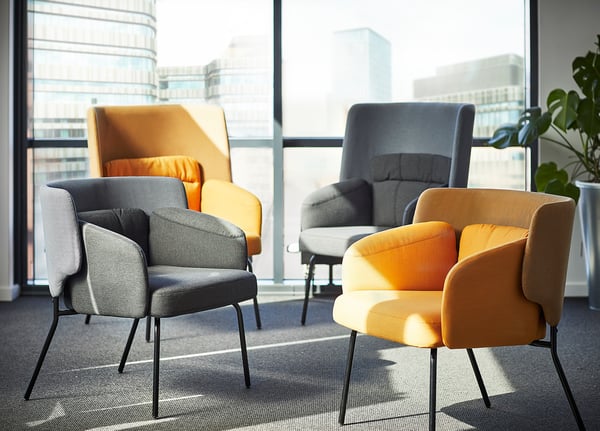 Modern office space with colourful, curved BINGSTA chairs in yellow and grey fabrics on dark carpet, with city view behind.