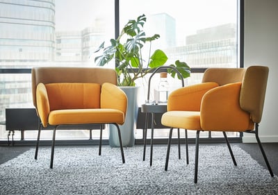 Modern interior with two bright orange BINGSTA armchairs, large plant, and city view.